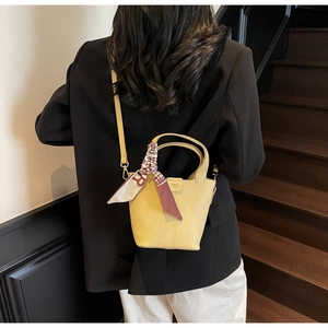 Detail view of yellow leather bucket bag with silk scarf on handle and pebbled texture