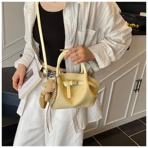 Detail of yellow crocodile embossed bucket bag with plush bear charm and strap