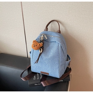 Detail of blue denim backpack with brown leather handles and a plush bear pendant