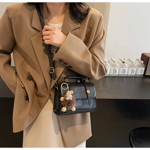 Detail of black leather square bag with golden hardware and brown plush monster charm