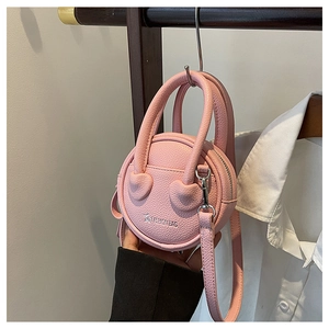 Detail of pink round mini crossbody bag featuring litchi texture and heart patches