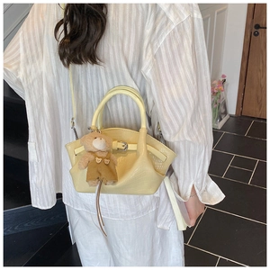Detail of light yellow crocodile pattern tote with a brown plush bear charm and strap