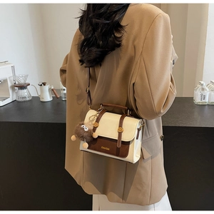 Detail view of vintage two-tone satchel bag with plush charm on beige blazer model