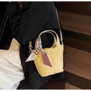Detail of yellow pebbled leather bucket bag with silk scarf and logo strap on model