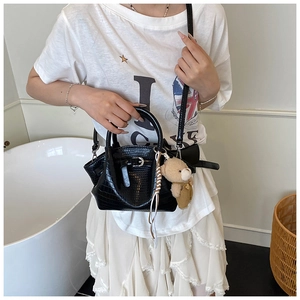 Detail of black crocodile texture handbag with plush bear charm and metal clasp