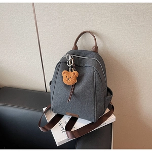 Close-up of a dark grey canvas backpack featuring a brown leather handle and cute bear charm