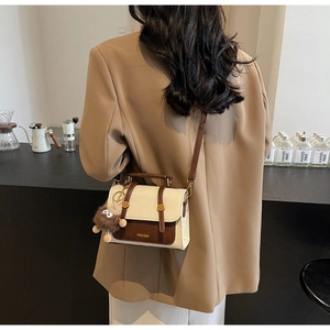Retro two-tone crossbody bag shown with a plush monster charm on a khaki blazer