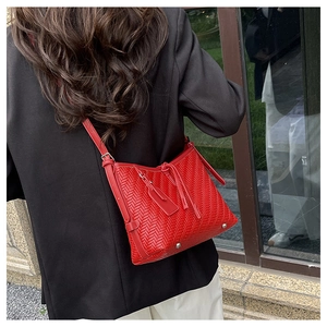 Detailed close-up of a vibrant red woven shoulder bag with stylish tassel and metal feet