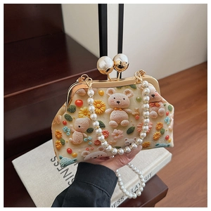 Detailed close-up of handmade crochet bear and floral pattern on cream-colored shell bag