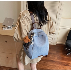 Rear view of light blue denim texture backpack with brown leather handle and teddy charm