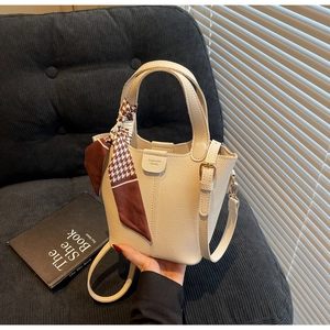Detail of cream bucket bag with lychee leather texture and decorative silk scarf handle