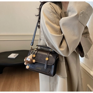 Detail of vintage dark brown crossbody bag with gold hardware and plush charm on trench coat