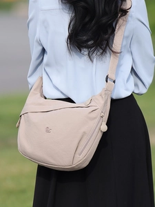 Minimalist beige canvas crossbody crescent bag shown on a model in an outdoor park setting