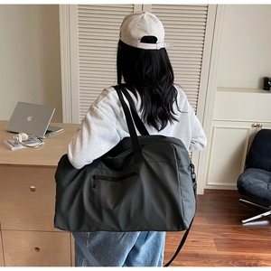 Dettaglio di una grande borsa da viaggio nera con manici robusti e tracolla su un modello