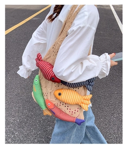 Detail of knit crochet tote bag featuring five colorful plush fish charms on street
