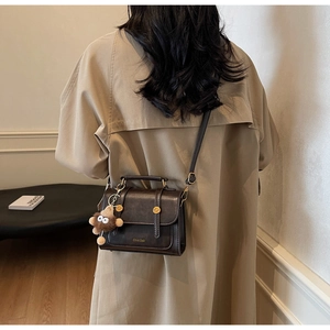 Detail of dark brown vintage handbag with gold hardware and plush lion charm on model