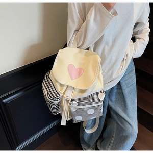 Detail of a yellow backpack with a pink heart patch and mixed pattern pockets on a model