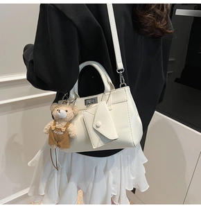 Femme portant un sac bandoulière blanc avec un pendentif ours et un fermoir métallique