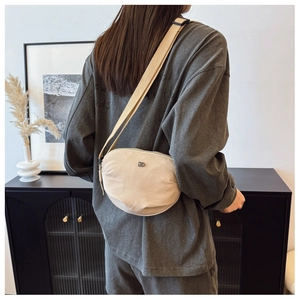 Lifestyle shot of a beige canvas half-moon crossbody bag with a metal logo on a model