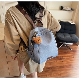 Detail of grey-blue canvas backpack featuring brown leather straps and cute bear pendant