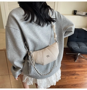 Chic cream croissant bag with dual straps showing detailed metal chain and knot texture
