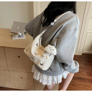 Détail d'un sac hobo crème avec bandoulière perlée et breloque en peluche sur un modèle