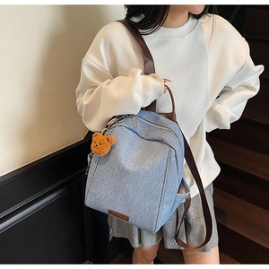 Close-up of blue canvas backpack featuring brown leather straps and a plush bear pendant