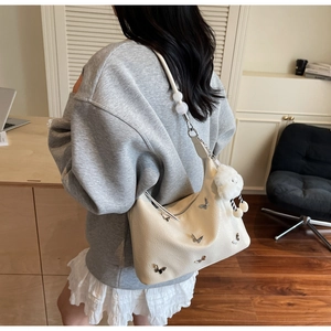 Détail du sac hobo avec papillon en métal et breloque mouton en peluche sur la bandoulière