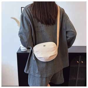Detail of a beige crescent crossbody bag with grain fabric texture and silver logo