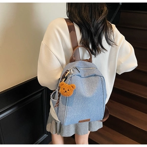 Detail of light blue denim texture backpack with brown leather strap and plush bear charm