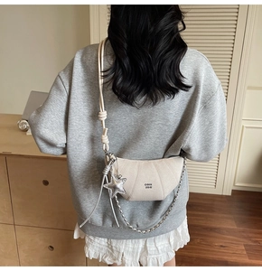 Detail of beige crescent bag with gold chain strap and star charm on a casual outfit