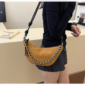 Detail of brown suede croissant bag with adjustable knot strap and decorative metal chain
