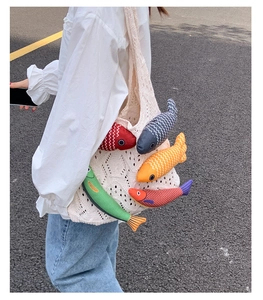 Detail of crochet tote bag featuring colorful plush fish charms worn by a model