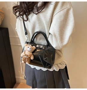 Détail d'un sac à main noir brillant avec fermoir argenté et charm ours en peluche
