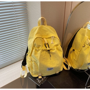 Detailed view of the bright yellow nylon backpack featuring side pockets and a white brand label