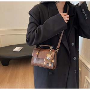 Detail showing vintage brown leather bag worn crossbody with furry charm accessory