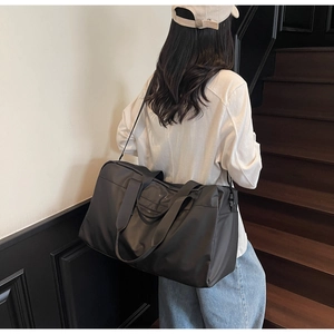 Vista posteriore di un modello con una grande borsa da viaggio nera con manici e tracolla