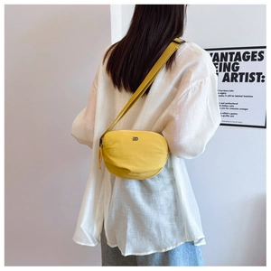 Minimalist bright yellow nylon crossbody bag shown worn by a model in a casual setting