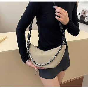 Detail view of beige half-moon bag with decorative chain and knotted black strap