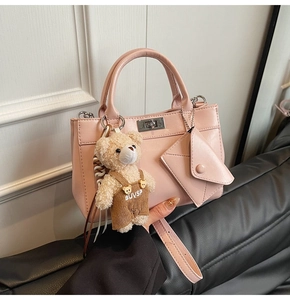 Détail d'un sac à main rose mat avec fermoir rotatif en métal et pendentif ours en peluche