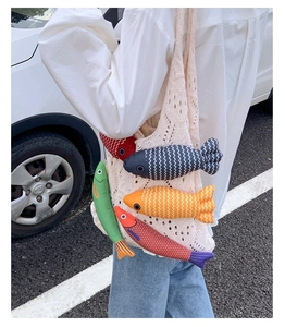Detail of crochet tote bag featuring five colorful plush fish charms in outdoor setting
