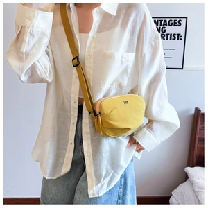 Detail view of yellow canvas crossbody bag with dual zippers and adjustable strap
