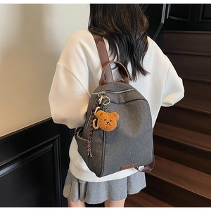 Detail of dark grey backpack with brown leather straps and a cute plush bear pendant