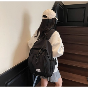 Side view of a minimalist black nylon backpack featuring a drawstring pocket and metal buckle