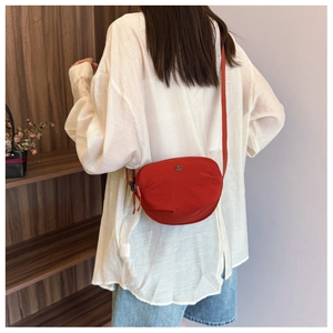 Detail of red nylon oval crossbody bag with adjustable strap and metal logo accent