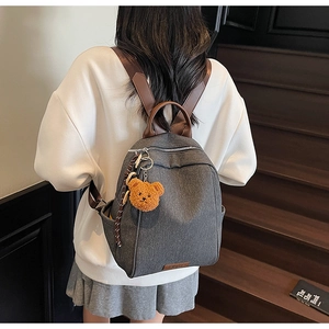Detail of dark grey backpack with brown straps and cute yellow bear plush charm detail