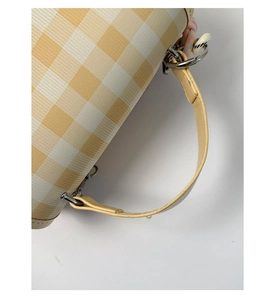 Detail of yellow checkered fabric texture and leather handle with metal D-rings on bag