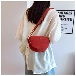 Detail of red nylon half-moon bag with adjustable strap worn by model in minimalist setting