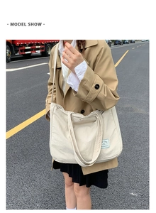 Outdoor model shot showing the large beige canvas tote bag worn as a crossbody bag