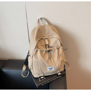 Detail of khaki nylon backpack featuring drawstring pocket and decorative metal carabiner